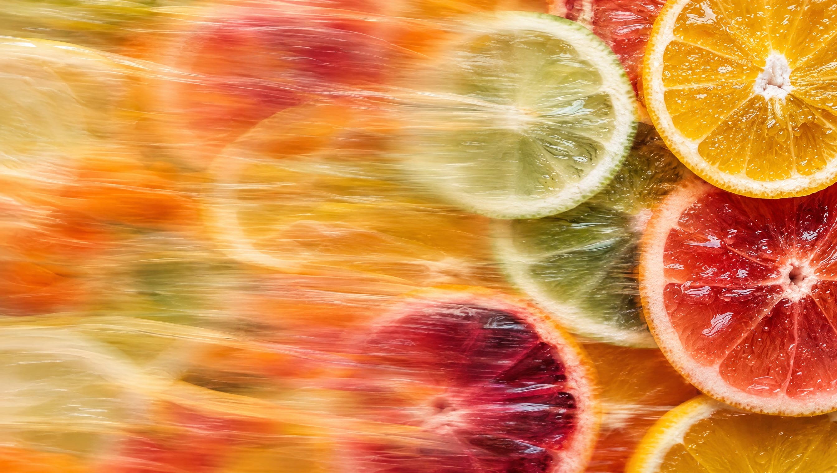 Slices of orange, lime, pink grapefruit and blood orange, close up, their colour pulled sideways into streaks of motion